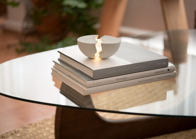 An open white Teno speaker sits atop a small stack of books on a glass coffee table.