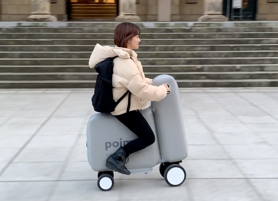 Young woman rides a Poimo inflatable scooter down the sidewalk. 