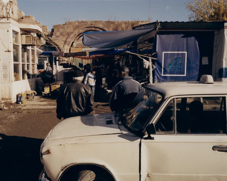 Armenian men rest against an old Lada car outside of a local market.