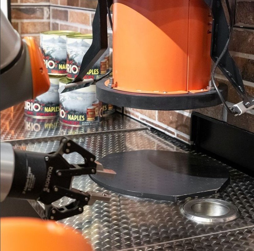 Pazzi's robotic arm presses dough while preparing a pizza.