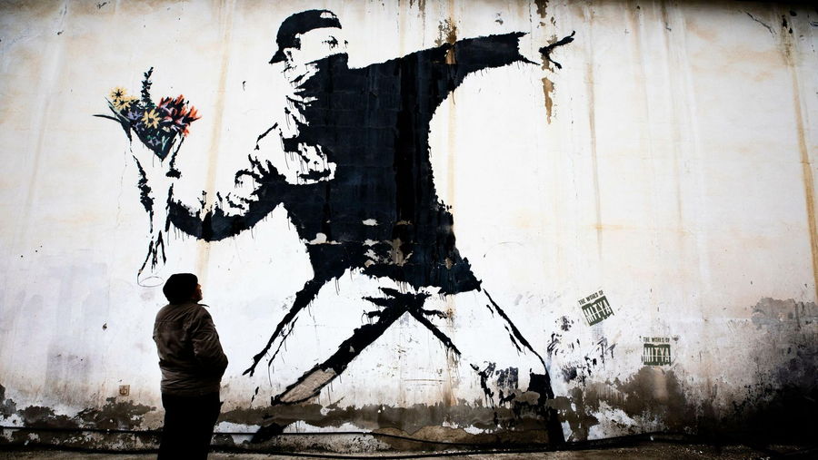 Large Banksy mural of protestor throwing a colorful bouquet of flowers. 