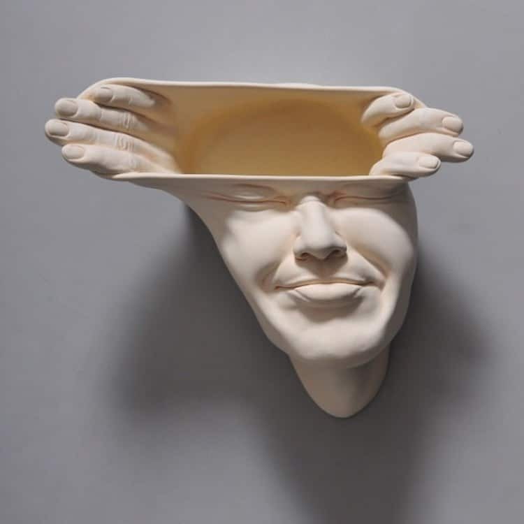 Surreal ceramic by Johnson Tsang shows a face being pushed and pulled apart by body-less hands.