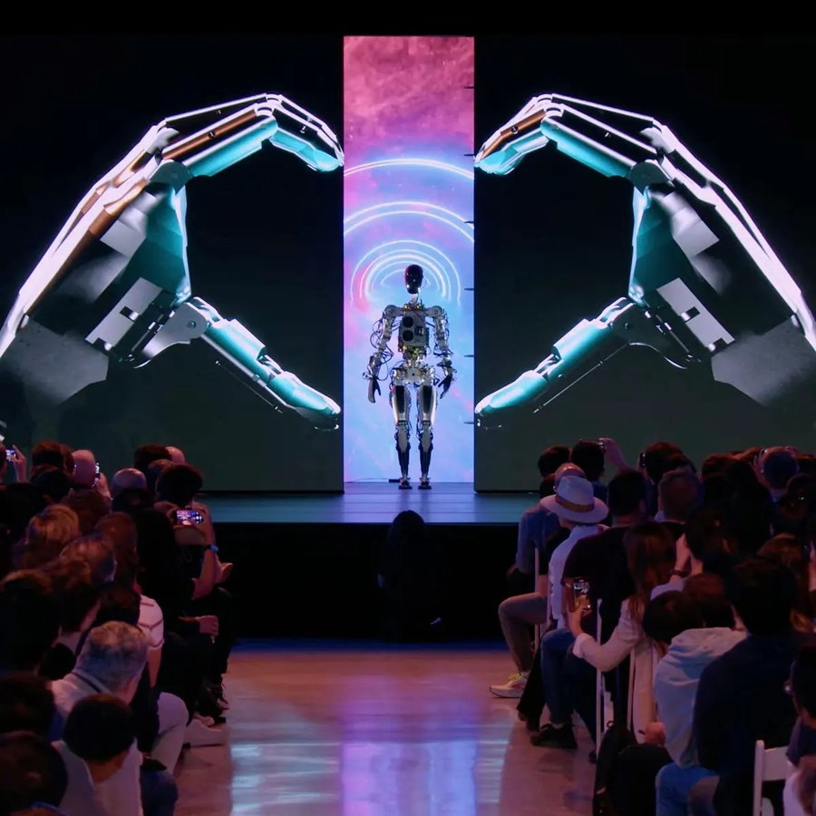 Tesla's humanoid Optimus robot stands in the middle of a heart made from robotic hands at Tesla AI Day 2022.