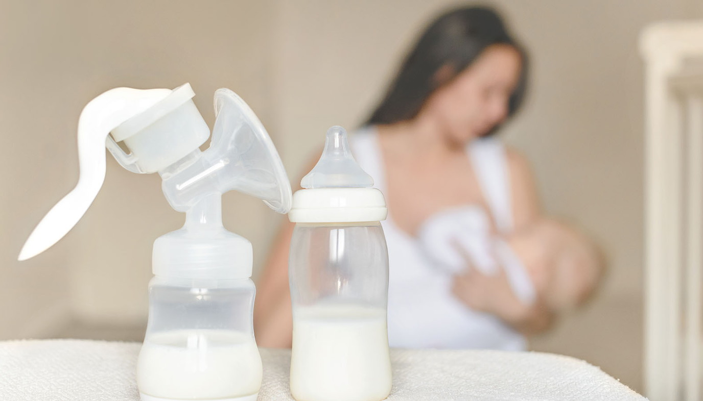 woman breastfeeding with breast milk nearby on table