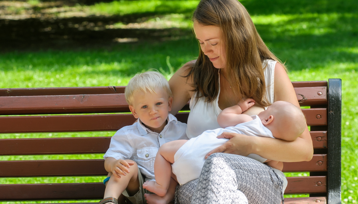 mother sitting on a bench breastfeeding her baby with her arm around other child