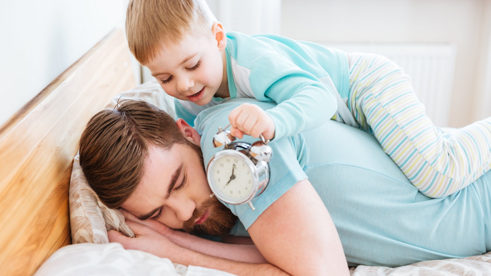 boy climbing on top of dad with an alarm clock
