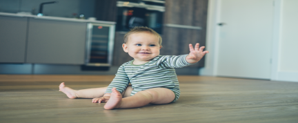 A toddler sitting on the floor waving. 
