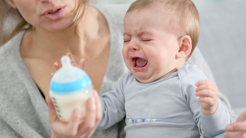 Crying baby with mother holding baby bottle