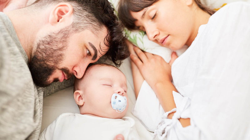 baby sleep with a pacifier between mom and dad