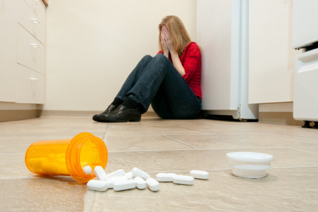 woman crying on the floor with open bottle of pills