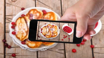 A woman holding an iPhone and taking a photograph of a plate of pancakes. 