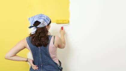 A woman paints a wall with yellow paint. 