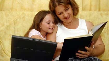 Mom and daughter working with laptop and a book.