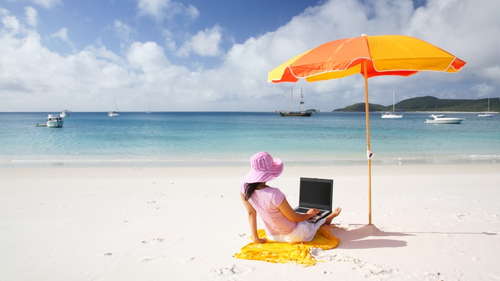A woman working on her laptop at the beach.