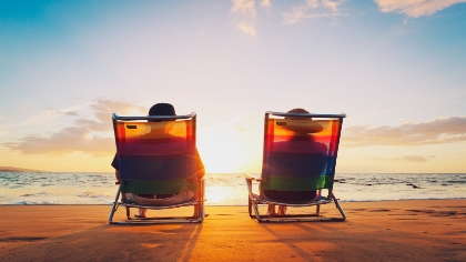 A retired couple sits on a beach together watching the sunset. 