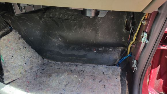Passenger floorboard with carpet pulled back.