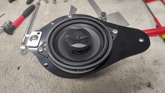 I traced the shape of the OEM mounting plate onto a piece of Lexan than then cut it out with my band saw and hole saw in a drill press.  I had to break off one of the 4 speaker mounting tabs to prevent interference with the speaker grill mounting slots.  I used a bracket I have for mounting things into slatwall which fit into the slot in the car to hold it perfectly.  Once I had the plate built, I covered it with some black vinyl so it would look good through the speaker grill.