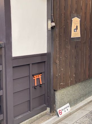The miniature torii, normally seen at Shinto shrines, is considered an entrance to a spiritual place. Here it is placed low on a building wall within an area with a lot of bars to prevent drunken guys from urinating on the building!
